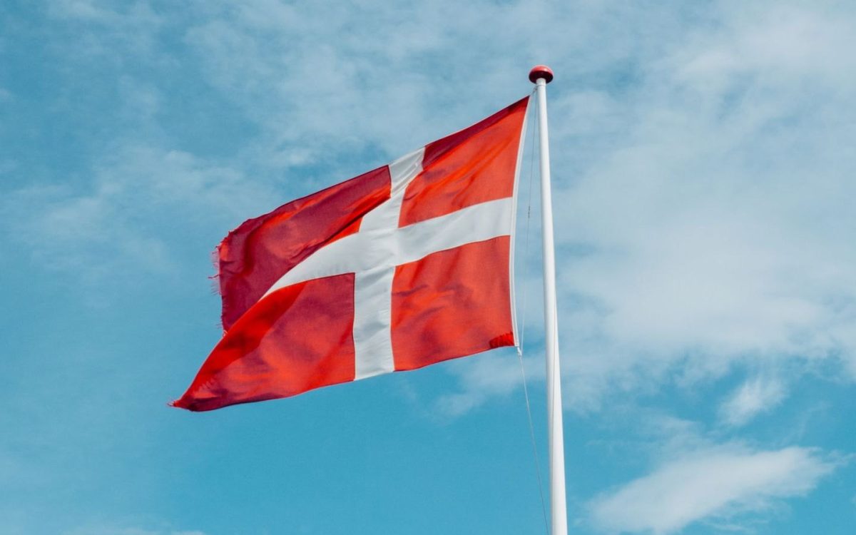 Dannebrog vajer fra en flagstang mod en blå himmel med lette skyer